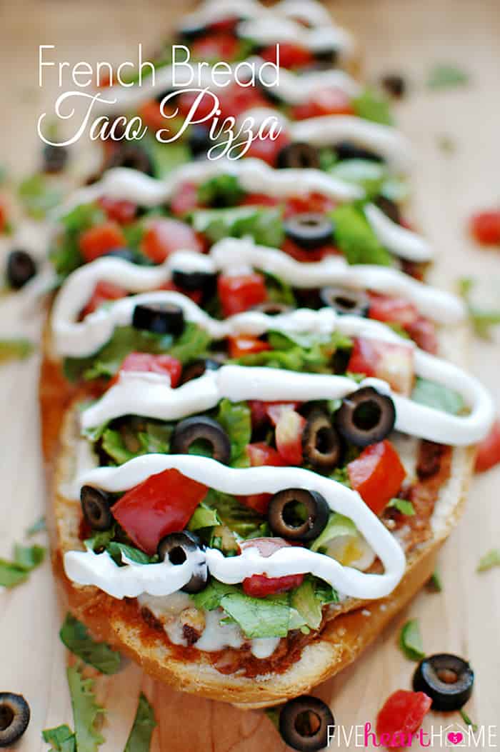 French Bread Taco Pizza ~ tacos meet pizza on an effortless French bread crust, with layers of refried beans, salsa, taco meat, cheese, lettuce, tomatoes, black olives, and sour cream! | FiveHeartHome.com