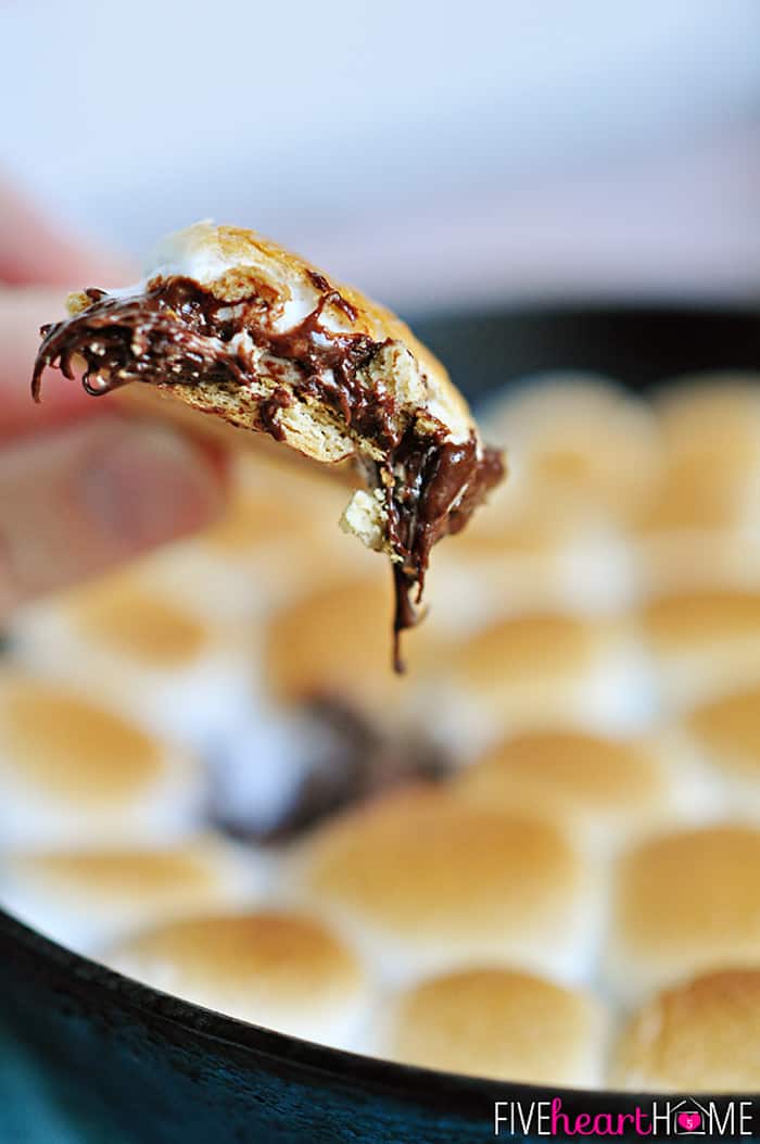 S'mores Dip ~ melted chocolate and toasty marshmallows bake up in a skillet; scoop up with graham crackers for a perfect party dessert! | FiveHeartHome.com Big bite of S'mores Dip on graham cracker.
