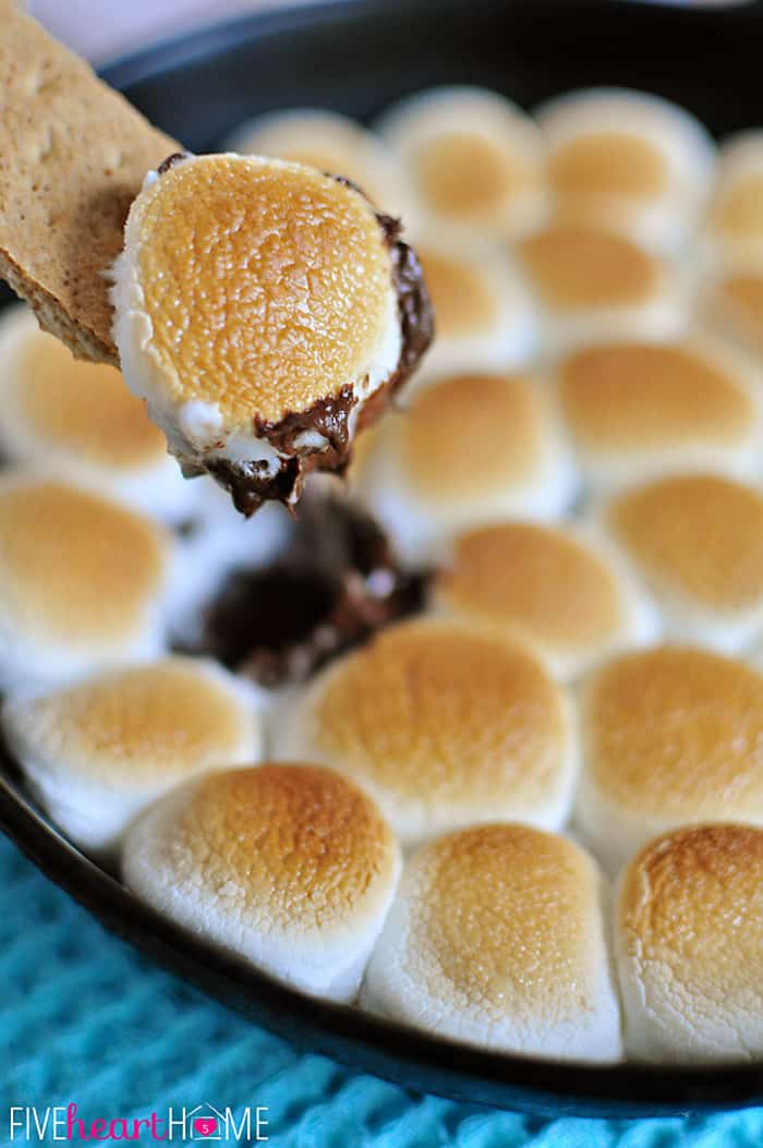 S'mores Dip ~ melted chocolate and toasty marshmallows bake up in a skillet; scoop up with graham crackers for a perfect party dessert! | FiveHeartHome.com Graham cracker dipping up toasted marshmallow and melted chocolate.