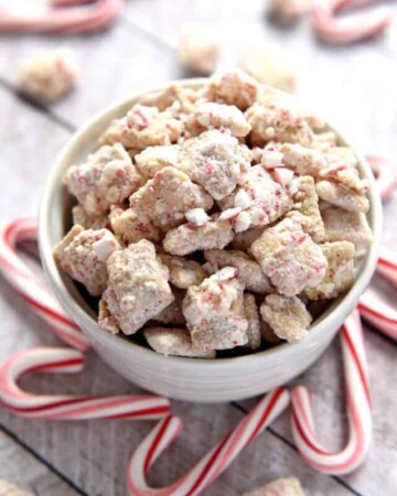 Christmas Puppy Chow in a bowl surrounded by candy canes.