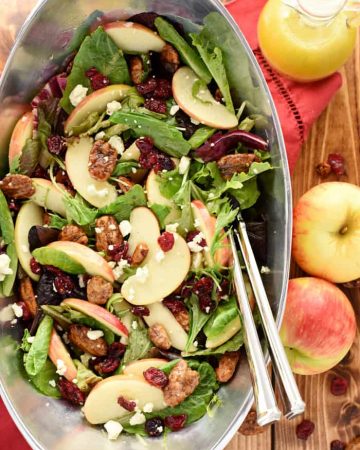 Aerial view of Holiday Honeycrisp Salad in pewter bowl with apples and dressing on table.