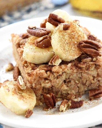Banana Baked Oatmeal on a plate garnished with sliced bananas, toasted pecans, and cinnamon.