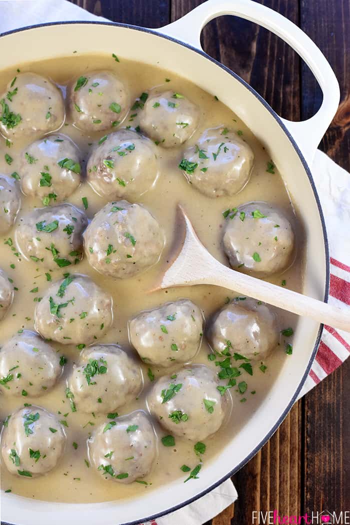 Aerial view of Swedish Meatballs and gravy in a skillet, with wooden spoon sticking out and garnished with fresh parsley