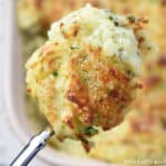 Make Ahead Mashed Potatoes, serving spoon suspended over baking dish.