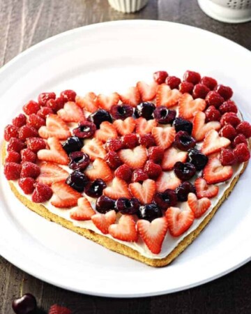Valentine's Day Fruit Pizza ~ featuring a tangy cream cheese frosting on a heart-shaped sugar cookie crust topped by sweet, glossy berries and cherries, this is the perfect Valentine's Day dessert recipe! | FiveHeartHome.com