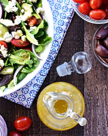 Aerial view of bottle of homemade Greek Dressing and a Greek salad.