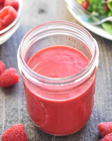 Jar of Raspberry Vinaigrette with salad and raspberries on table.