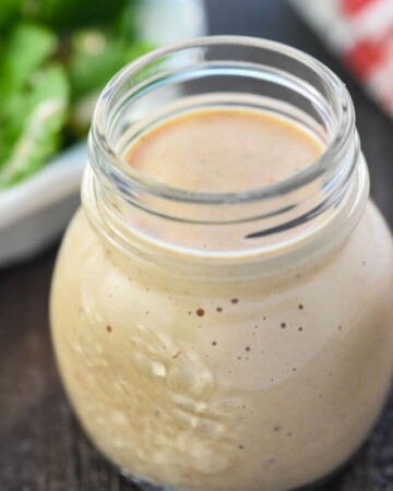 Homemade Thousand Island Dressing in glass jar with salad in background.
