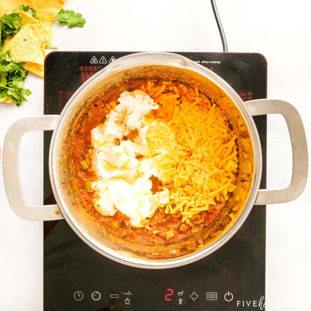 Stirring cream cheese and grated cheddar into Beef Enchilada Dip mixture.