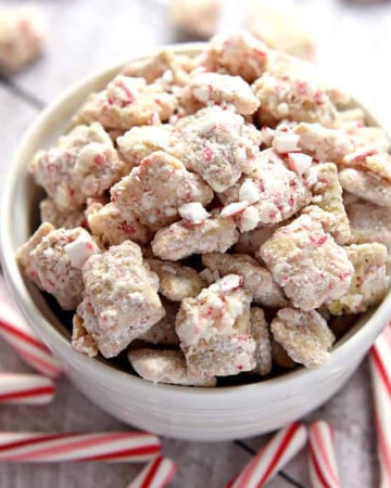 Christmas Puppy Chow (or Christmas Muddy Buddies) in a bowl surrounded by candy canes.